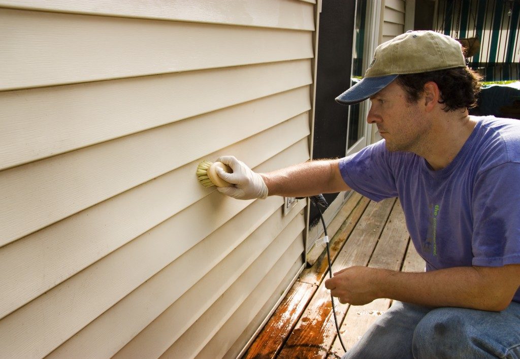 Man cleaning vinyl siding with a brush