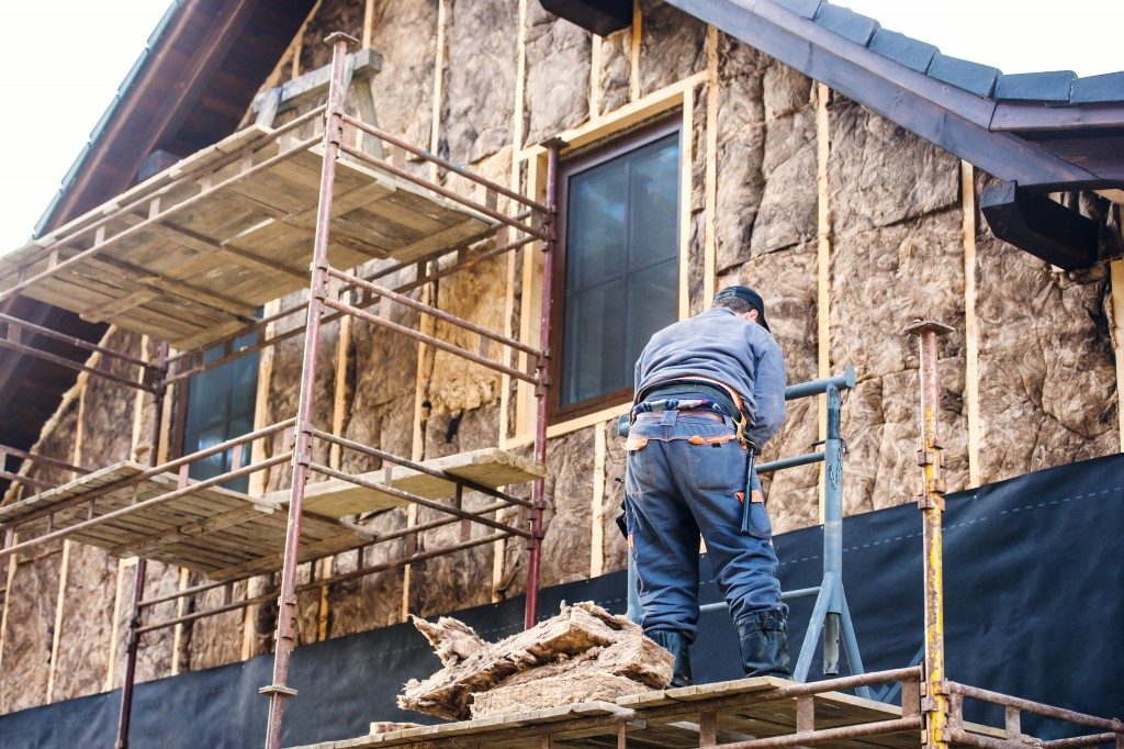 Construction worker thermally insulating house facade with glass wool