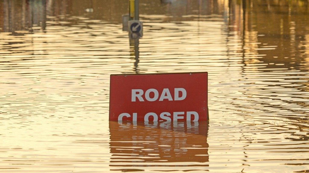 A 'Road Closed' sign partially covered in flood water lit by the evening sun